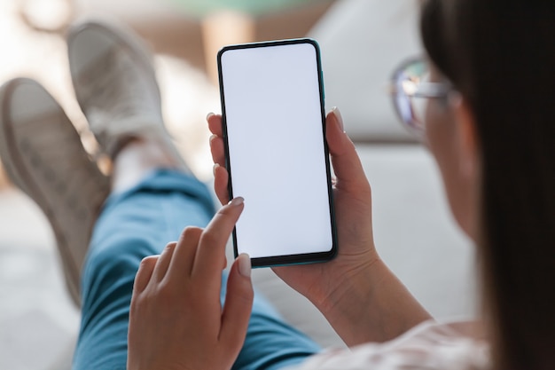 Mulher segurando o celular nas mãos, deitada no sofá