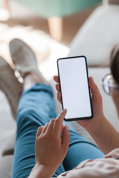 Mulher segurando o celular nas mãos, deitada no sofá