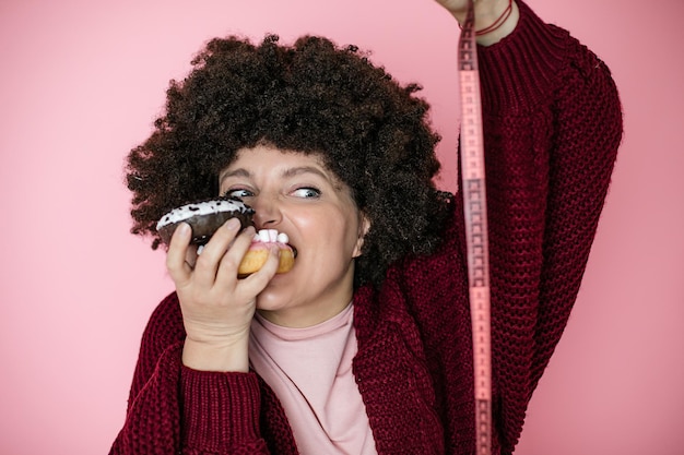 Mulher segurando o donut na mão e verificar sua gordura corporal com fita métrica. humor foto, diversão, alegria, dieta, conceito de vício