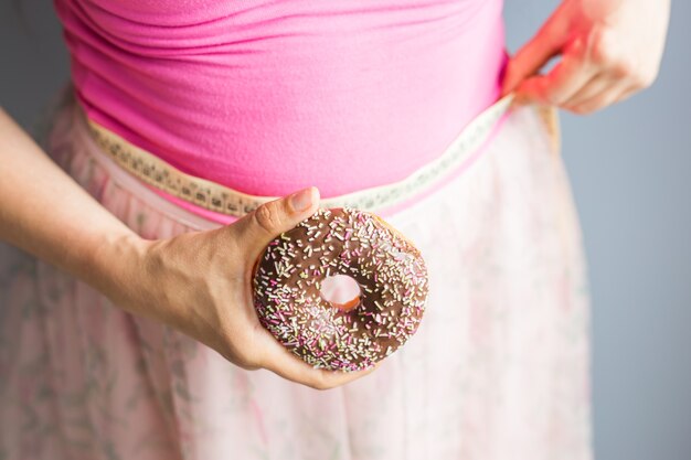 Mulher segurando o donut na mão e verificar sua gordura corporal com fita métrica.