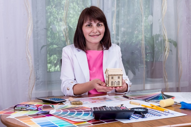 Mulher segurando o modelo da casa nas mãos sobre os desenhos