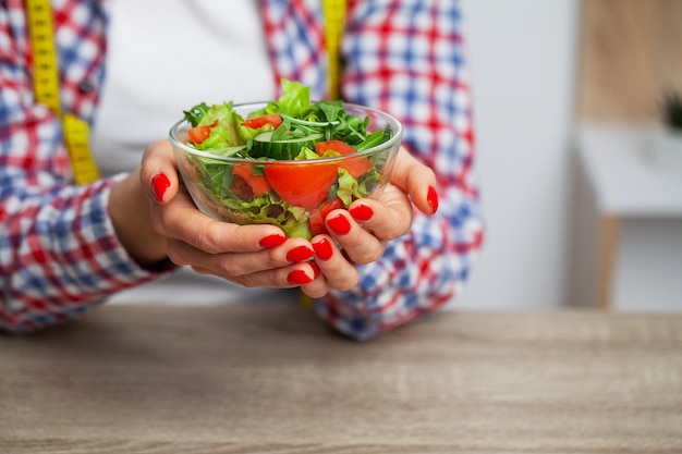 Mulher segurando salada de legumes fresca em um prato transparente