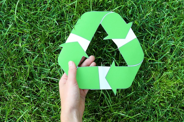 Mulher segurando símbolo de reciclagem contra grama verde