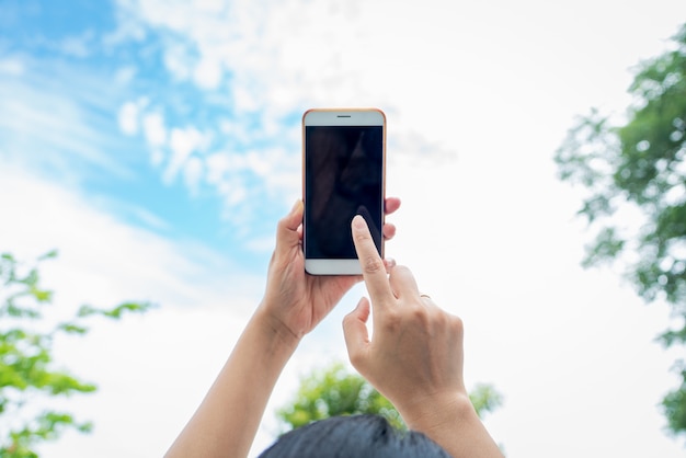 Mulher segurando smartphone com fundo de céu desfocado