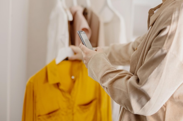 Mulher segurando smartphone e tirando foto de suas roupas velhas para vendê-las online vendendo no site ecommerce reutilize o conceito de segunda mão estilo de vida sustentável do consumidor consciente vista de perto