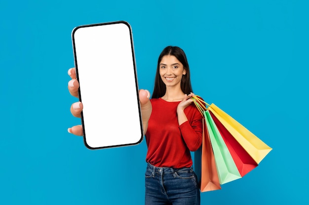 Mulher segurando smartphone em branco e sacos de compras