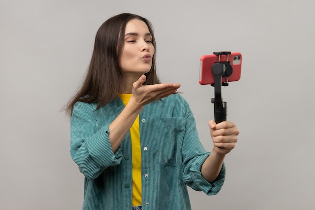 Mulher segurando smartphone na câmera estável transmitindo transmissão ao vivo ou fazendo selfie mandando beijo no ar