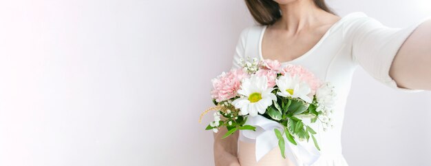 Mulher segurando um buquê de flores do casamento e tirar selfie sobre um fundo claro.