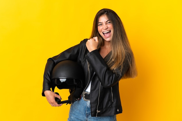 Mulher segurando um capacete de motociclista isolado em amarelo comemorando uma vitória