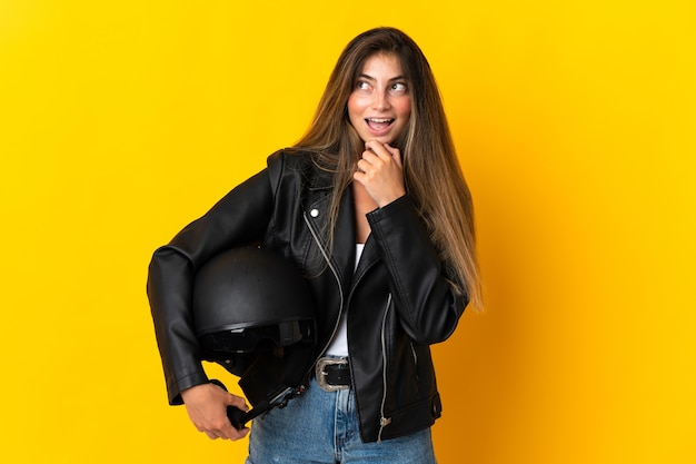 Mulher segurando um capacete de motociclista isolado em amarelo, olhando para o lado e sorrindo