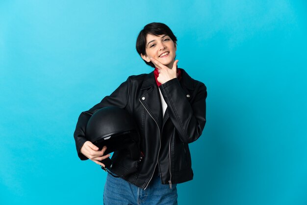 Mulher segurando um capacete de motociclista isolado na parede azul feliz e sorridente