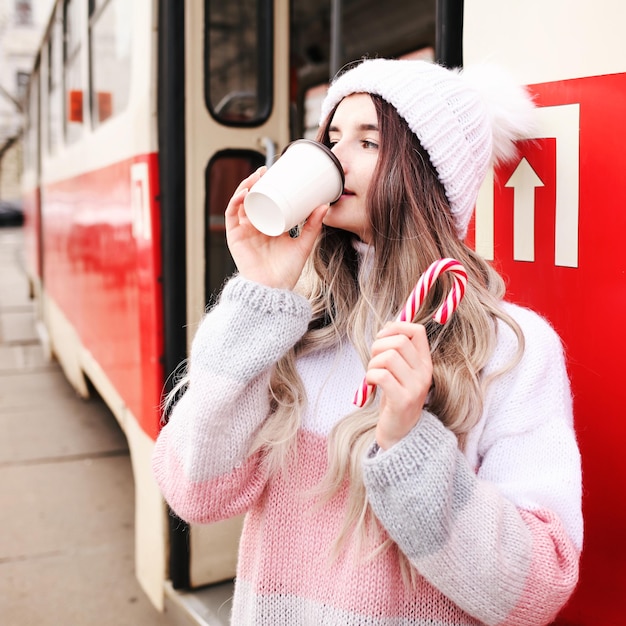 Mulher segurando um copo de papel e bebendo café enquanto espera o trem