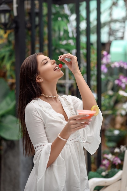 Mulher segurando um coquetel e uma cereja nas mãos