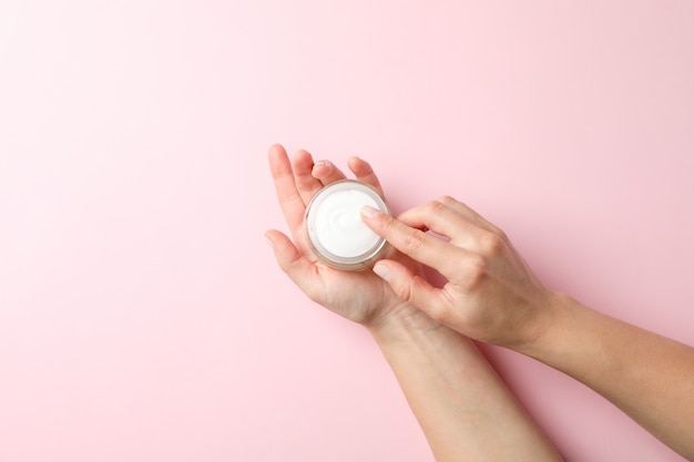 Mulher segurando um frasco de creme de inverno para pele em fundo rosa