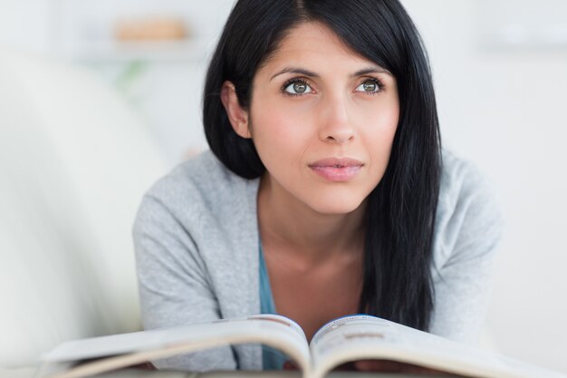 Mulher segurando um livro em suas mãos enquanto estava deitada em um sofá