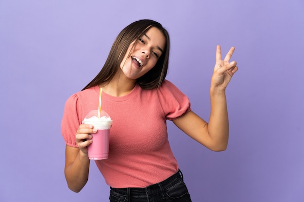 mulher segurando um milkshake de morango sorrindo e mostrando o sinal da vitória