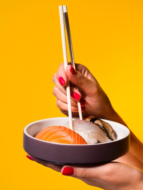 Mulher segurando um prato com sushi em um fundo amarelo