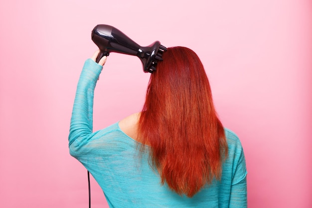 Mulher segurando um secador de cabelo em um fundo rosa