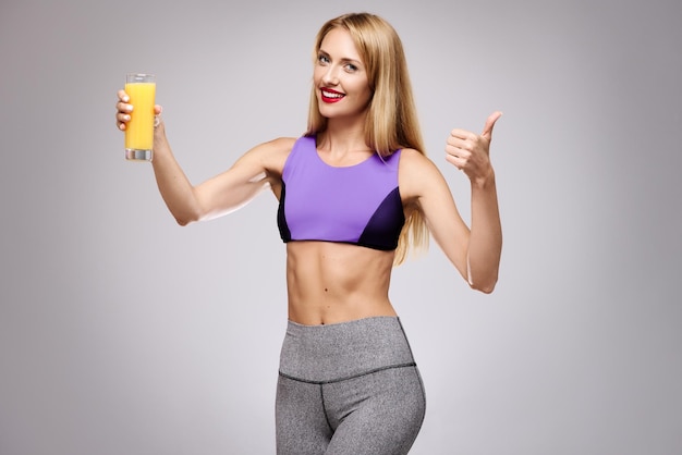 Foto mulher segurando um suco de laranja e mostrando o polegar para cima o conceito de uma dieta saudável