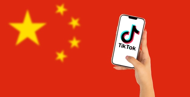 Mulher segurando um telefone celular com o logotipo TikTok com a bandeira da China ao fundo