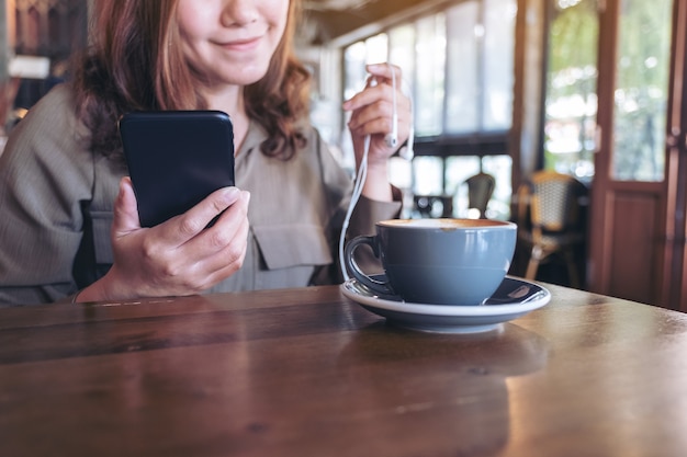 mulher segurando um telefone celular e fones de ouvido enquanto ouve música no café