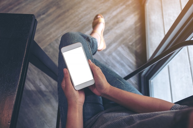 Mulher segurando um telefone inteligente branco com uma tela em branco enquanto está sentada no café