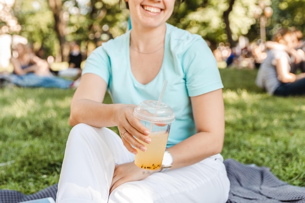 Mulher segurando uma bebida fresca no parque da cidade turva fundo anjo largo
