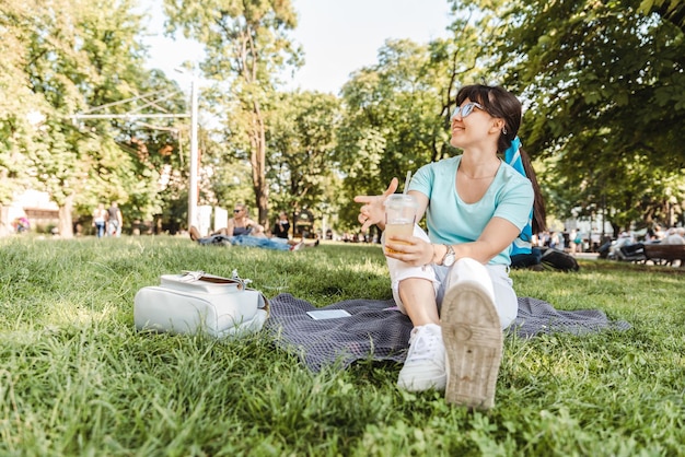 Mulher segurando uma bebida fresca no parque da cidade turva fundo anjo largo