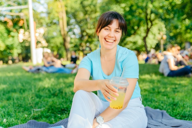 Mulher segurando uma bebida fresca no parque da cidade turva fundo anjo largo