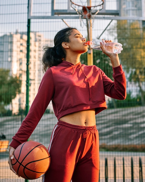 Mulher segurando uma bola de basquete e bebendo água