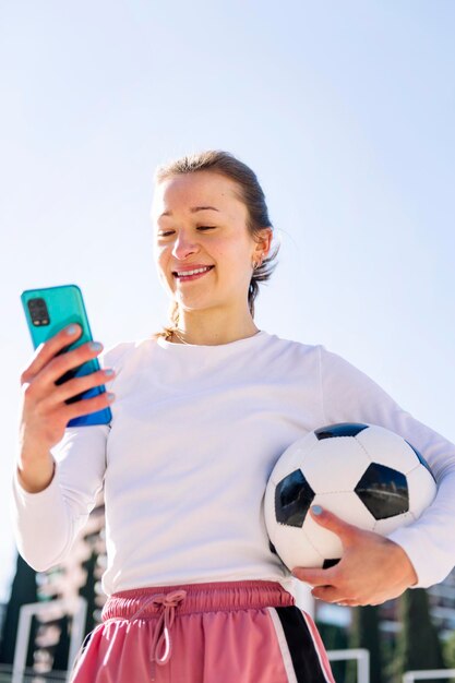 Mulher segurando uma bola de futebol enquanto usa telefone celular