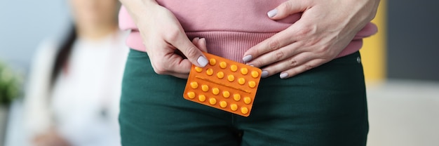 Mulher segurando uma bolha com comprimidos na parte inferior do abdômen em closeup clínica