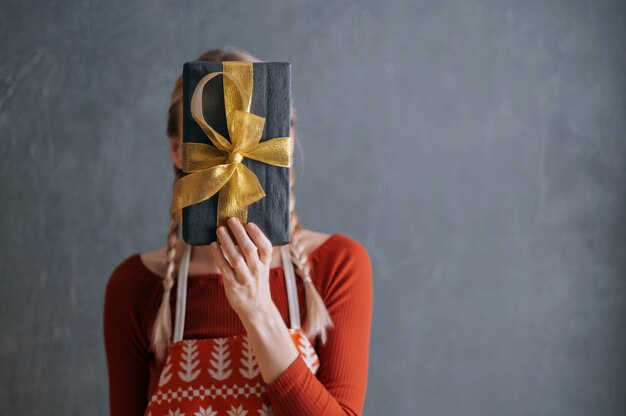 Mulher segurando uma caixa com um presente de Natal nas mãos na frente do rosto