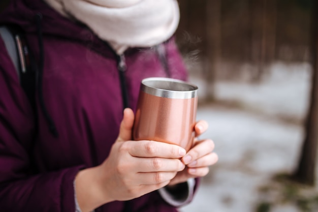 Mulher segurando uma caneca térmica com chá quente e fumegante nas mãos