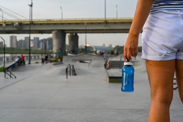 Foto mulher segurando uma garrafa de água depois de andar em um parque extremo. a pista de skate, patins, rampas de quarter e half pipe. esporte radical, cultura urbana jovem para atividades de rua adolescentes.