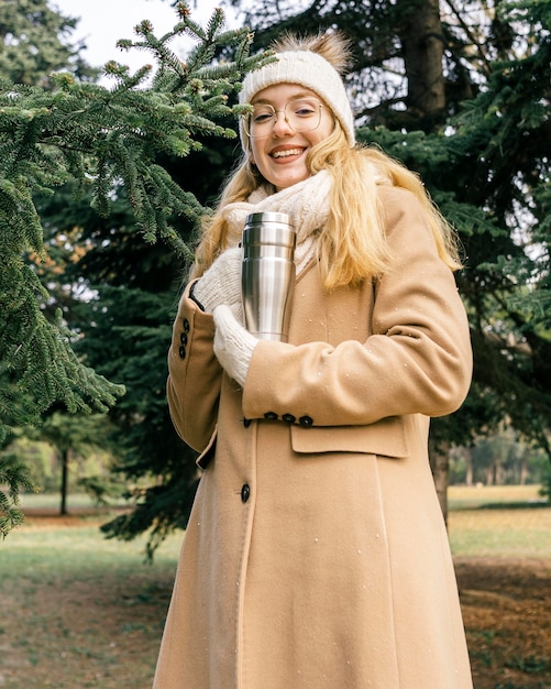 Mulher segurando uma garrafa térmica no parque no inverno