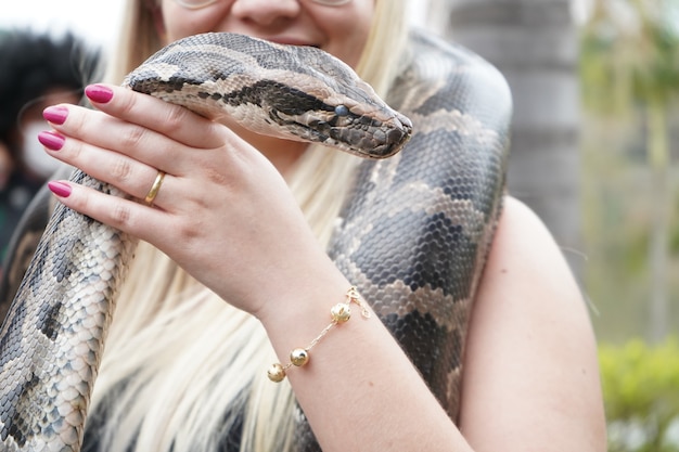 Mulher segurando uma grande cobra nos braços e nas mãos