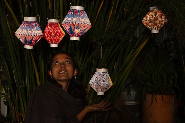 Mulher segurando uma lanterna de papel colorida enquanto olha para outras lanternas penduradas em uma planta