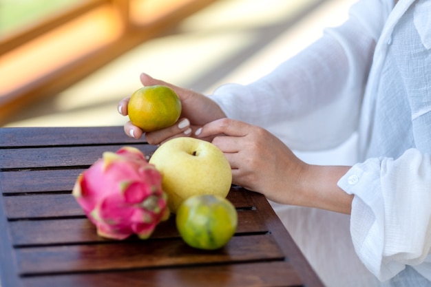 Foto mulher segurando uma laranja com pêra e fruta do dragão em uma pequena mesa de madeira