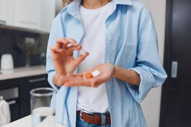 Mulher segurando uma pílula de pé em frente a um copo de água pronta para tomar medicação para tratamento de saúde