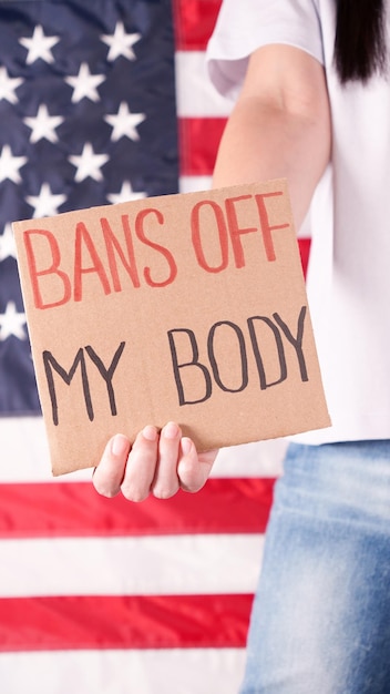 Mulher segurando uma placa de proibições fora do meu corpo Bandeira americana no fundo