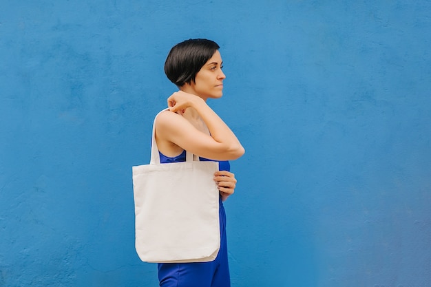 Mulher segurando uma sacola de lona em um fundo azul brilhante na cidade. Saco ecológico reutilizável. Conceito ecológico.