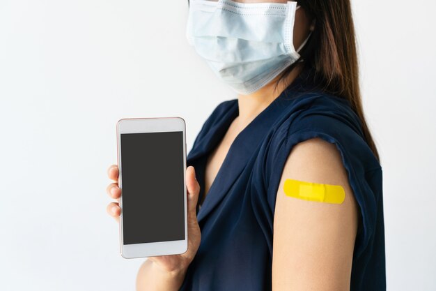 Mulher segurando uma tela em branco do telefone móvel após a injeção da vacina covid-19. copie o espaço