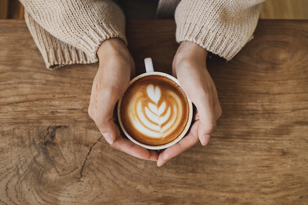 Mulher segurando uma xícara de café com leite quente no conceito de bebida matinal de mesa de madeira