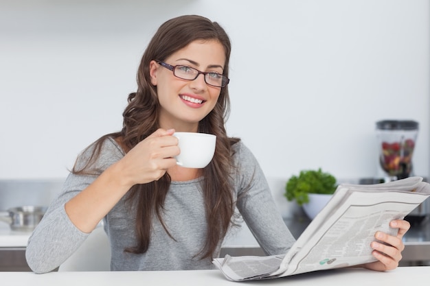 Mulher segurando uma xícara de café enquanto lê um jornal