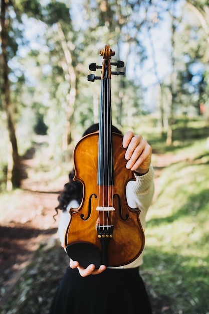 Mulher segurando violino em pé na floresta Sessão vertical