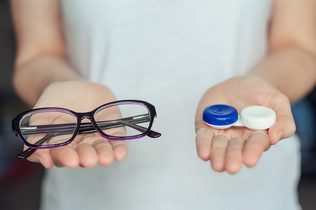Mulher segurar lentes de contato e óculos nas mãos. conceito de escolha da proteção da visão