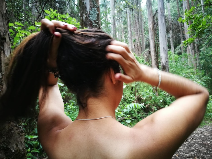 Foto mulher sem camisa amarrando o cabelo na floresta