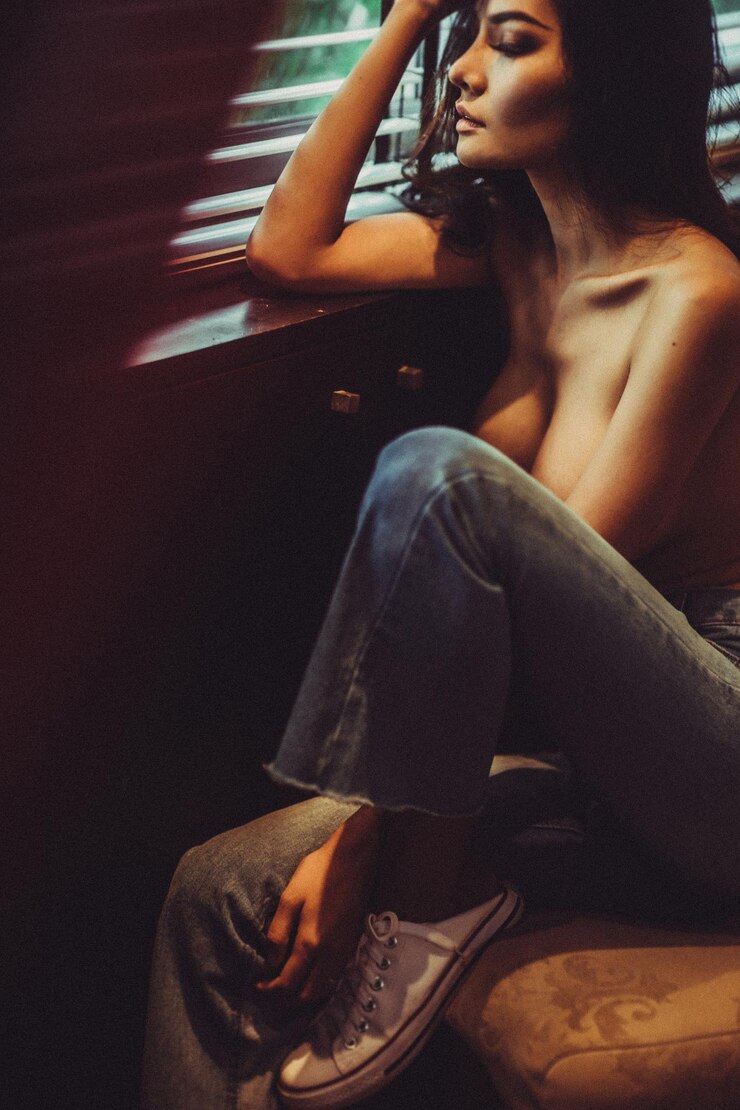 Foto mulher sem camisa olhando pela janela enquanto está sentada em casa