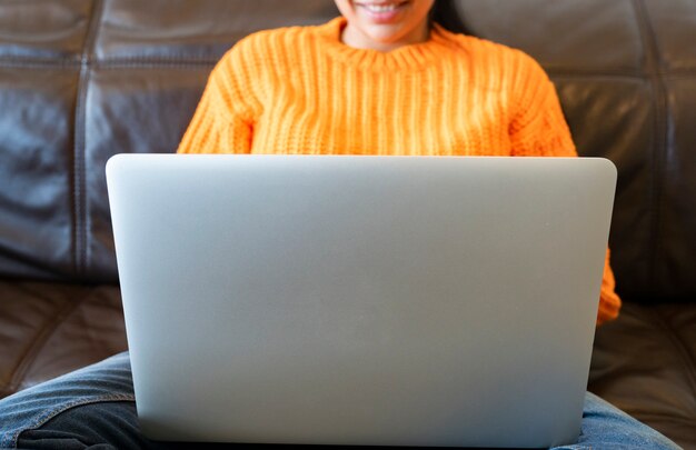 Mulher sem rosto usando computador no sofá em casa